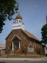 Photo of a modest brown brick church with a central entry beneath a cupola. 